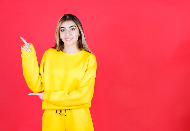 Foto grátis retrato de uma jovem com roupa amarela em pé na parede vermelha