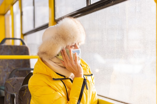 Retrato de uma jovem com roupas quentes em um ônibus urbano em um dia de inverno com um telefone celular na mão