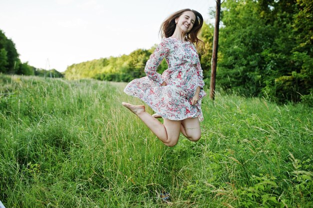 Retrato de uma jovem deslumbrante de vestido pulando no prado