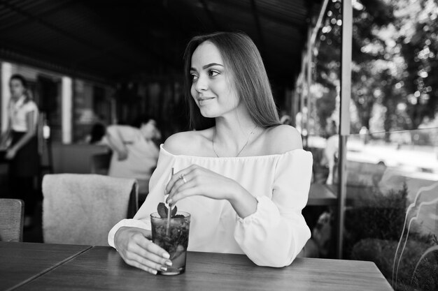 Retrato de uma jovem deslumbrante posando com coquetel de mojito no café ao lado do parque Foto em preto e branco