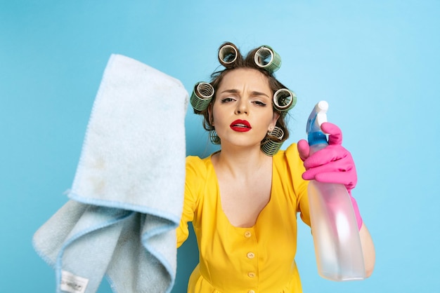 Retrato de uma jovem elegante lavando janelas com spray de limpeza isolada sobre fundo azul