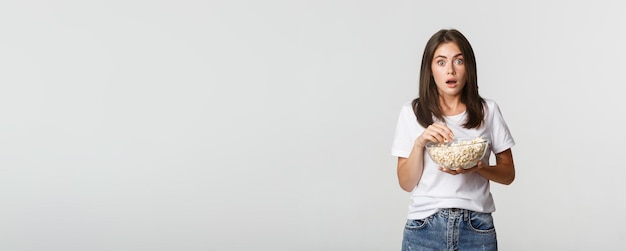 Retrato de uma jovem emocionada e espantada comendo pipoca e assistindo filmes ou séries de tv