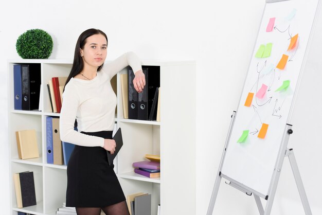 Retrato de uma jovem empresária, apoiando-se na prateleira no local de trabalho