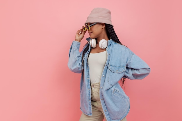 Foto grátis retrato de uma jovem estilosa com fones de ouvido brancos em óculos de sol da moda posando isolado sobre fundo rosa do estúdio