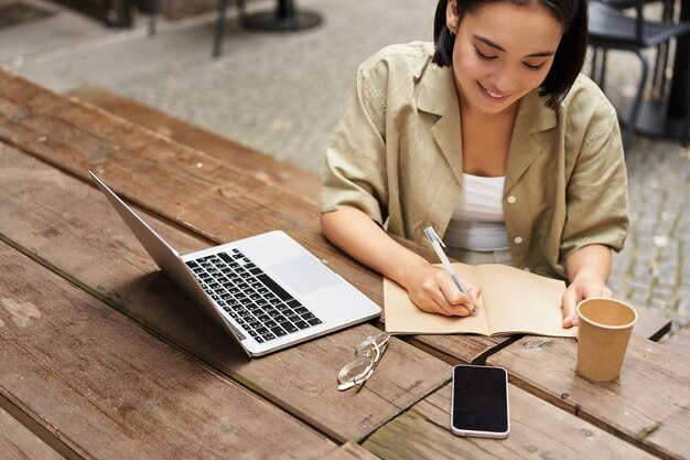 Retrato de uma jovem estudando online sentada com laptop anotando e olhando para