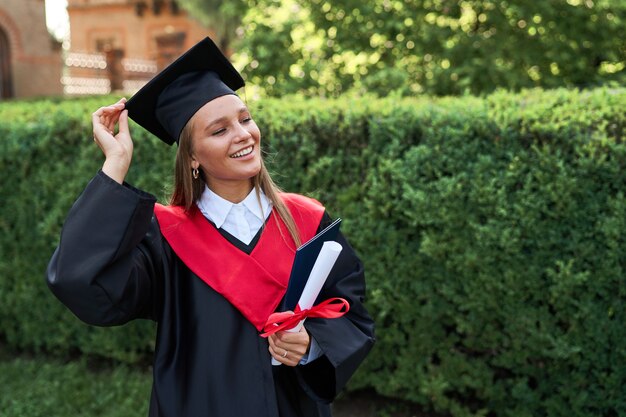 Retrato de uma jovem estudante de pós-graduação bonita com túnica de formatura e diploma