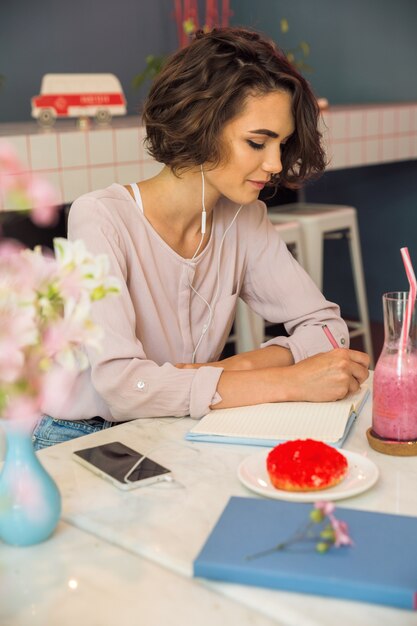 Retrato de uma jovem estudante em fones de ouvido escrevendo notas