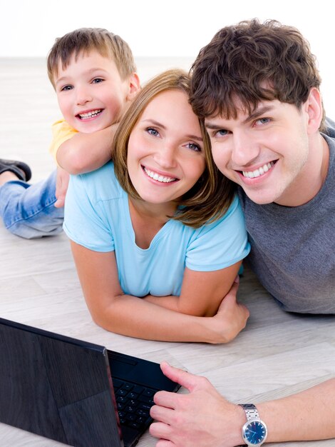 Retrato de uma jovem família feliz rindo com o filho pequeno e com laptop - dentro de casa