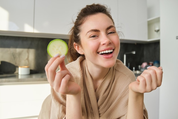 Foto grátis retrato de uma jovem feliz e sorridente na cozinha cozinhando cortando abobrinha segurando legumes