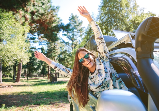 Retrato de uma jovem feliz levantando os braços pela janela do carro em um dia ensolarado