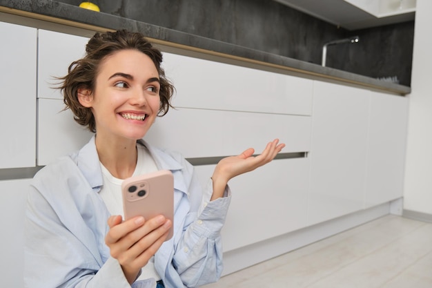 Foto grátis retrato de uma jovem feliz mostra sua nova cozinha sentada em pontos de chão em móveis e