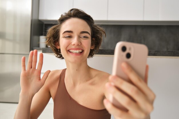 Retrato de uma jovem fitness sentada em casa no tapete de borracha grava vídeo em smartphone fazendo trabalho