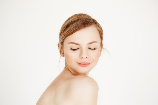 Retrato de uma jovem garota bonita nua com pele limpa saudável, sorrindo, olhando para baixo. Tratamento facial.