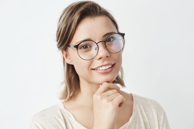 Retrato de uma jovem garota linda de óculos sorrindo segurando a mão no queixo.