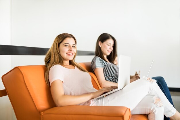 Retrato de uma jovem latina sentada no sofá com o colega na parte de trás com o laptop