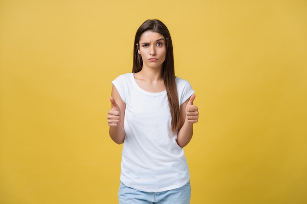 Retrato de uma jovem linda e alegre garota sorrindo olhando para a câmera sobre fundo amarelo Gesto dos polegares para cima