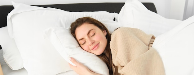 Foto grátis retrato de uma jovem linda e feliz descansando na cama de pijama abraçando seu travesseiro e