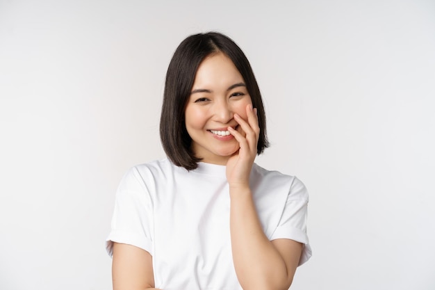 Retrato de uma jovem linda garota coreana rindo e sorrindo parecendo coquete em pé contra o fundo branco