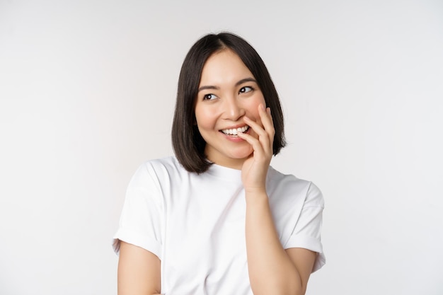 Retrato de uma jovem linda garota coreana rindo e sorrindo parecendo coquete em pé contra o fundo branco