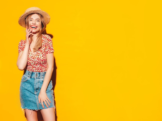 Retrato de uma jovem linda loira sorridente em roupas da moda de verão mulher despreocupada posando perto da parede amarela no estúdio Modelo positivo se divertindo dentro de casa Alegre e feliz no chapéu