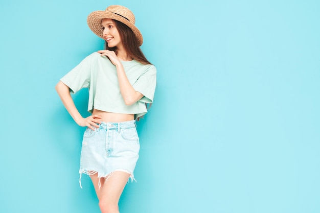 Retrato de uma jovem linda mulher sorridente na moda verão jeans saia mulher despreocupada posando perto da parede azul no estúdio Modelo positivo se divertindo dentro de casa Alegre e feliz no chapéu