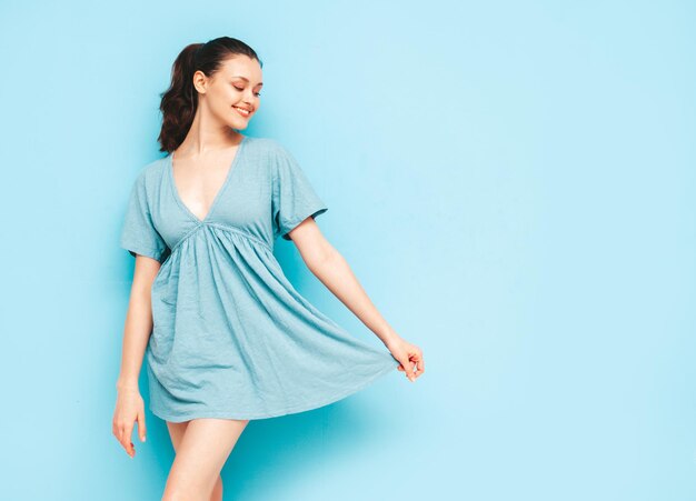 Retrato de uma jovem linda mulher sorridente no vestido azul de verão na moda Mulher despreocupada sexy posando perto da parede azul no estúdio Modelo positivo se divertindo e enlouquecendo Alegre e feliz