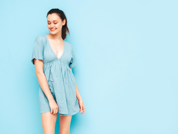 Retrato de uma jovem linda mulher sorridente no vestido azul de verão na moda Mulher despreocupada sexy posando perto da parede azul no estúdio Modelo positivo se divertindo e enlouquecendo Alegre e feliz