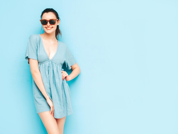 Retrato de uma jovem linda mulher sorridente no vestido azul de verão na moda Mulher despreocupada sexy posando perto da parede azul no estúdio Modelo positivo se divertindo e enlouquecendo Alegre e feliz