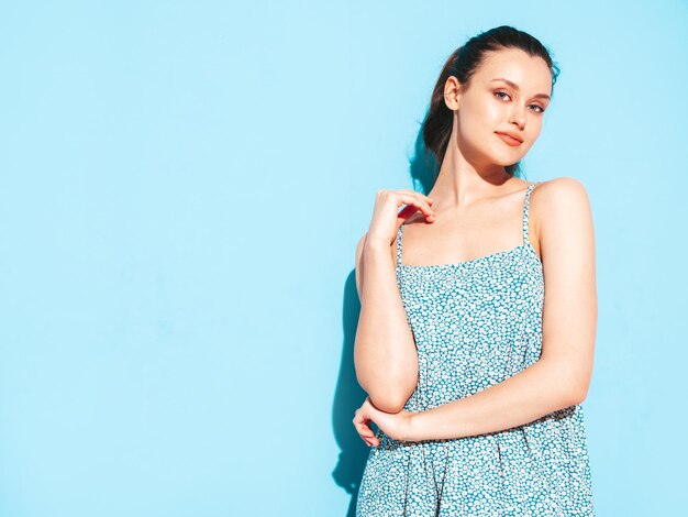 Retrato de uma jovem linda mulher sorridente no vestido azul de verão na moda Mulher despreocupada sexy posando perto da parede azul no estúdio Modelo positivo se divertindo e enlouquecendo Alegre e feliz