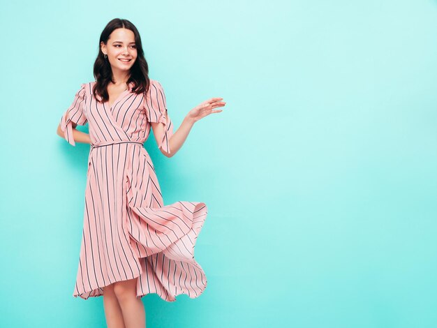 Retrato de uma jovem linda mulher sorridente no vestido rosa de verão na moda Mulher despreocupada sexy posando perto da parede azul no estúdio Modelo positivo se divertindo dentro de casa Alegre e feliz