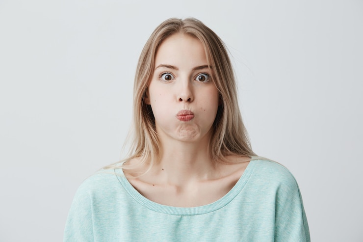 Foto grátis retrato de uma jovem loira chocada e espantada, com olhos arregalados, vestido casualmente, fazendo beicinho nas bochechas, como se estivessem cheias de água, recusando-se a contar segredo. fazendo caretas caucasiano modelo feminino.