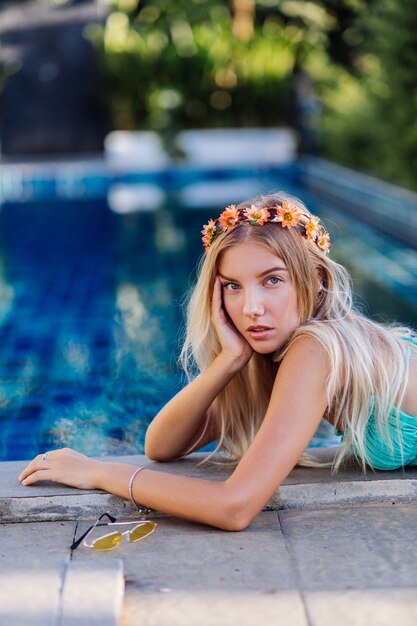 Retrato de uma jovem loira feliz de cabelos longos, biquíni azul e coroa de flores na cabeça