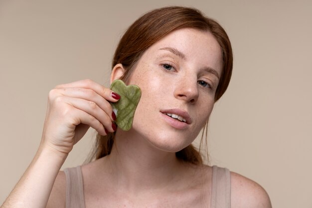 Retrato de uma jovem massageando o rosto usando um gua sha