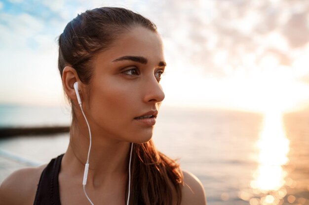 Retrato de uma jovem menina morena linda esportiva ao nascer do sol na beira-mar. Copie o espaço.