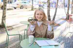 Foto grátis retrato de uma jovem modelo urbana sentada em um café ao ar livre gravando uma mensagem de voz com perturbação