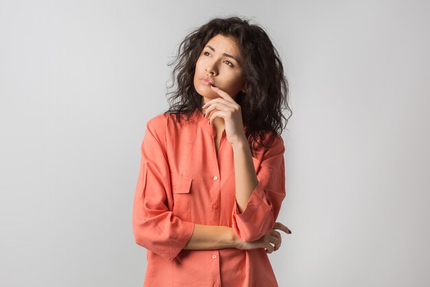 Retrato de uma jovem morena pensativa em uma camisa laranja, cabelo encaracolado, estilo verão, expressão de rosto frustrado, emoção triste, olhando de lado, pensando, problema, ideia, raça mista, isolado