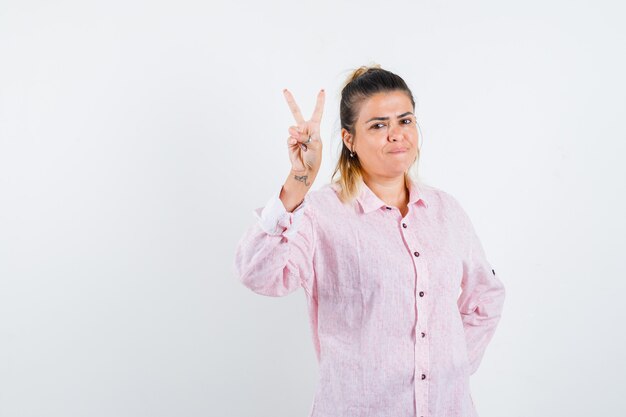 Retrato de uma jovem mostrando o V-sign de camisa rosa e olhando de frente com confiança