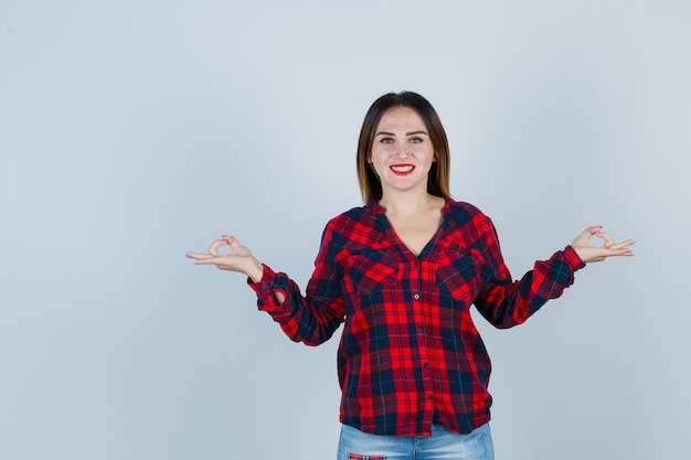 Retrato de uma jovem mostrando um gesto de mudra em uma camisa xadrez e olhando para a frente alegre