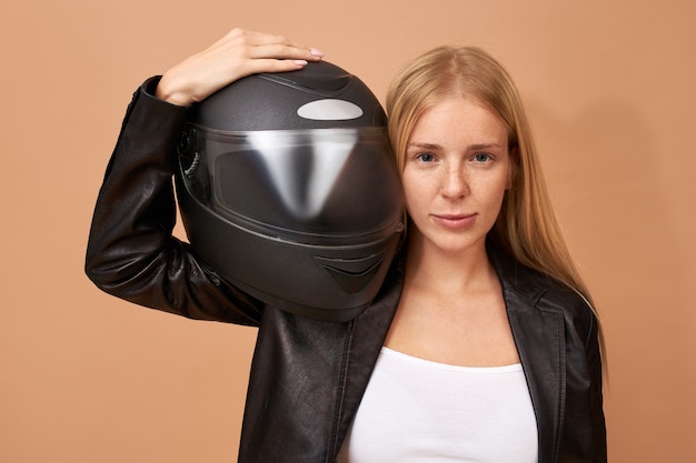 Retrato de uma jovem motociclista muito feliz com aparelho dentário e cabelo longo e reto posando isolada em uma jaqueta de couro preta