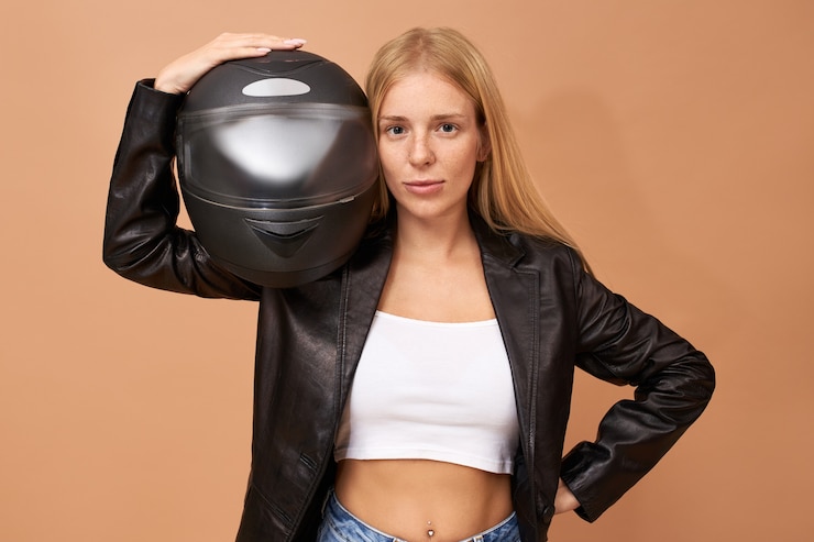 Foto grátis retrato de uma jovem motociclista muito feliz com aparelho dentário e cabelo longo e reto posando isolada em uma jaqueta de couro preta