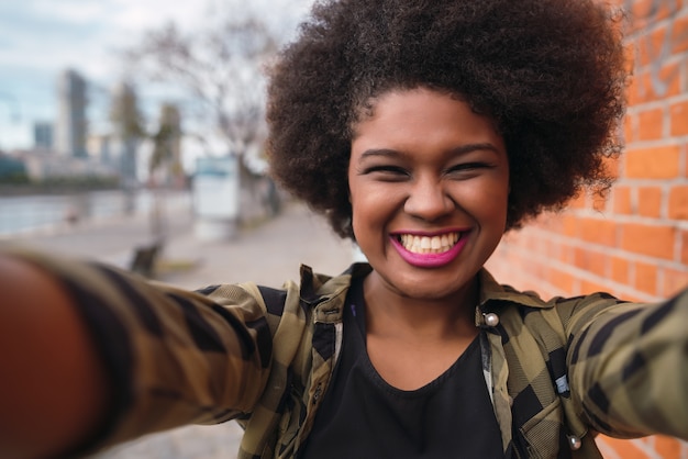 Foto grátis retrato de uma jovem mulher afro-americana linda tomando uma selfie ao ar livre na rua.