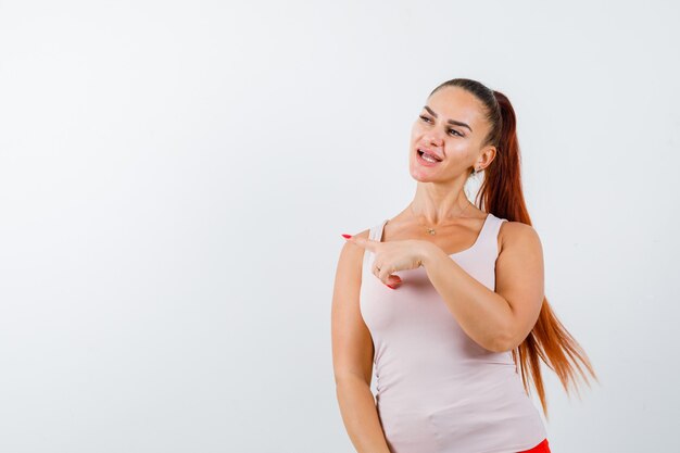 Retrato de uma jovem mulher apontando para o canto superior esquerdo em uma camiseta e olhando de frente com confiança
