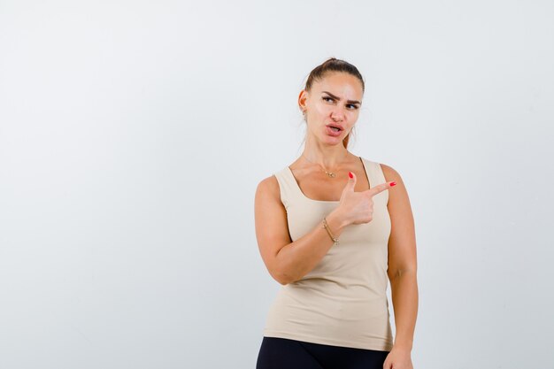 Retrato de uma jovem mulher apontando para o lado direito em um top bege e olhando atenciosamente para a frente