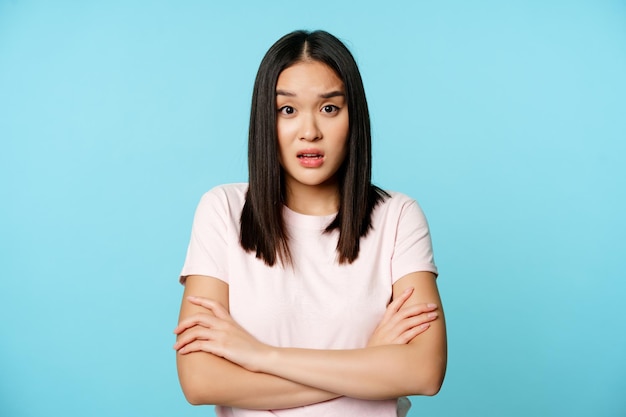 Retrato de uma jovem mulher asiática ouvindo com expressão confusa de rosto chocado em pé na camiseta ove ...