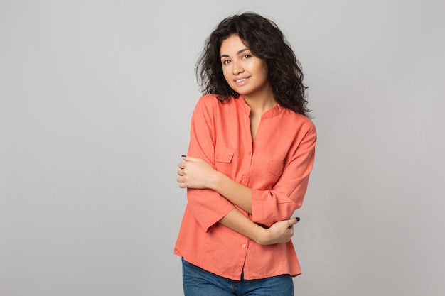 Retrato de uma jovem mulher atraente com camisa de algodão laranja, cabelo encaracolado, tímida, sorridente, feliz, abraçando-se, aparência natural, estilo de verão, tendência da moda,, mestiça, isolado