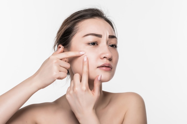 Retrato de uma jovem mulher atraente, tocando seu rosto e procurando acne, isolado na parede branca