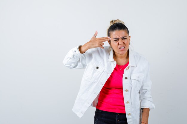 Retrato de uma jovem mulher bonita fazendo gesto de suicídio em uma camiseta, jaqueta branca e parecendo irritada com a vista frontal