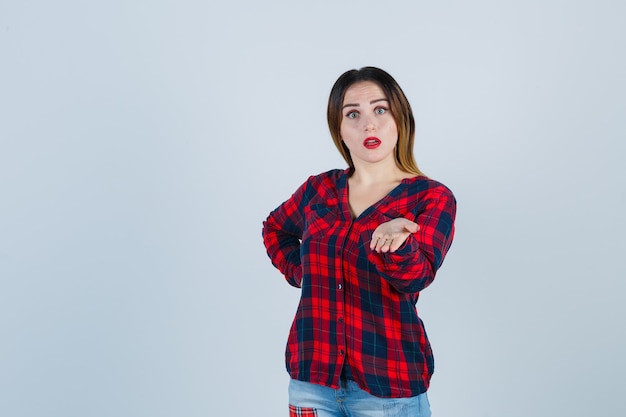 Retrato de uma jovem mulher bonita fingindo segurar algo em uma camisa casual e olhando a vista frontal chocada