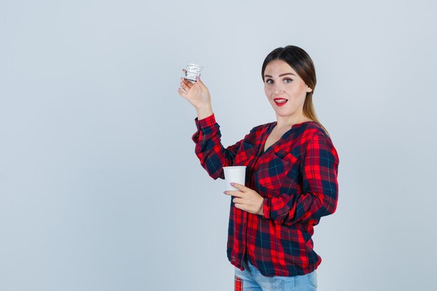 Retrato de uma jovem mulher bonita segurando óculos de plástico em uma camisa casual, jeans e olhando frontalmente bem-aventurada