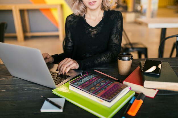 Retrato de uma jovem mulher bonita sentada à mesa com uma camisa preta, trabalhando no laptop em um escritório colaborativo